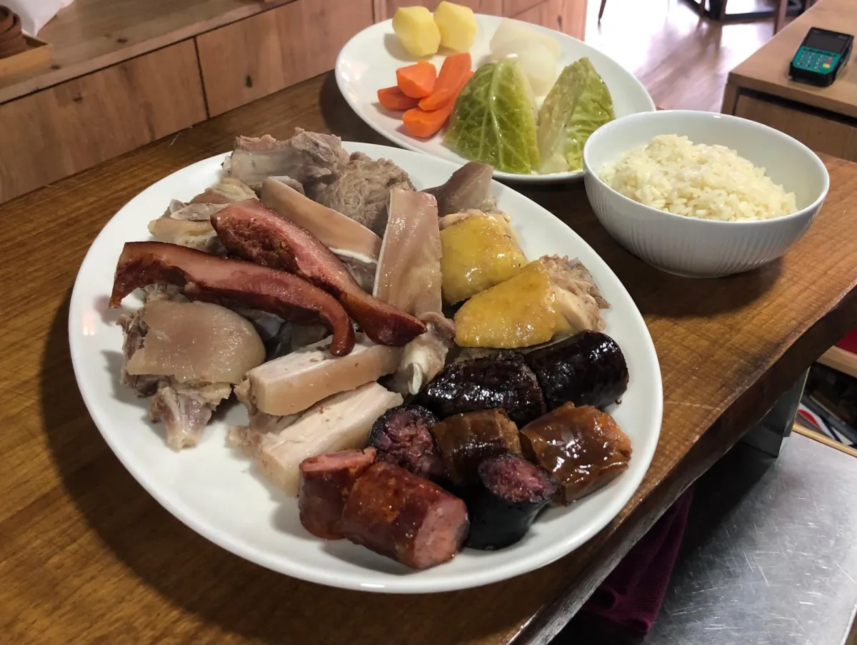 Mesa completa com cozido, acompanhamentos e vinho no Fogo e Tradição