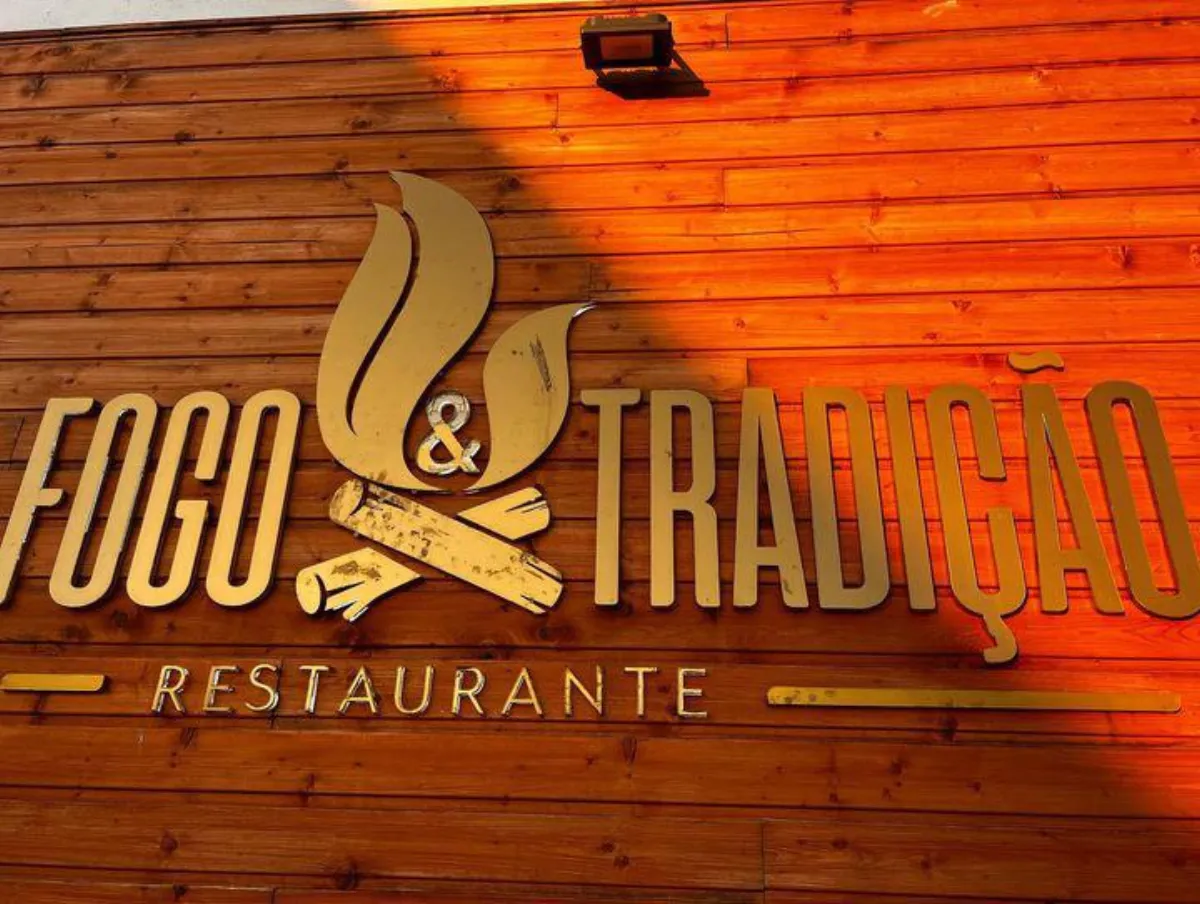 Fachada do restaurante Fogo e Tradição à noite com letreiro iluminado
